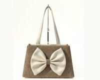 Neutral-toned structured handbag with double handles and a large ivory bow detail on the front, displayed on a minimalist background.